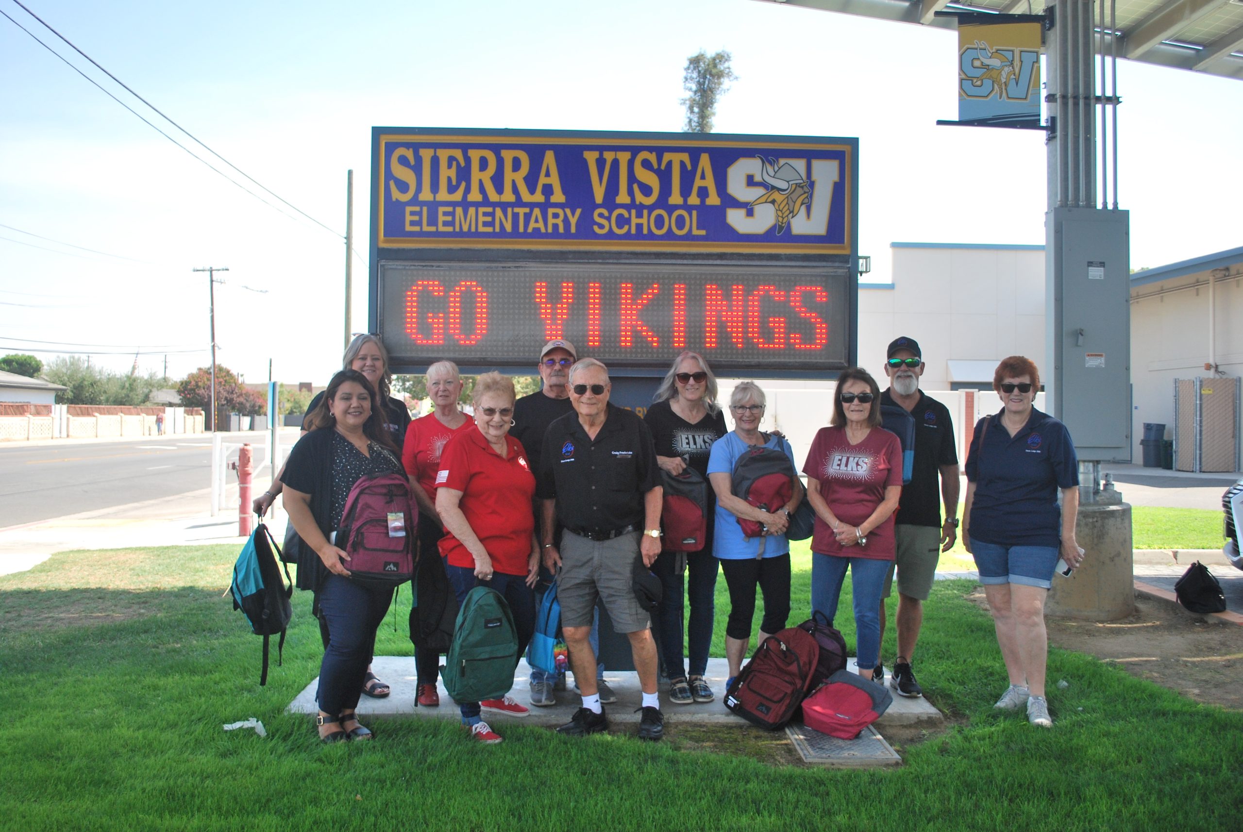 Members of the Elks Lodge and officials from the Clovis Unified School District posing with some of the backpacks they donated to Sierra Vista Elementary School (photo by Hannah-Grace Leece, Clovis Roundup). Back row from left to right: Tacy Kroell (CUSD representative), Pat Krueger, Steve Majors, Darcie Majors, David Sexauer, Marti Fredricks. Front row: Mellisa Arredondo (CUSD representative) Barbara McKinley, Craig Fredricks, Linda Navarro, Pati Soto.